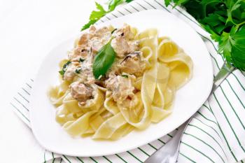Tagliatelle pasta with salmon, cream, garlic and herbs in a plate on a kitchen towel, fork, parsley and basil on white wooden board background