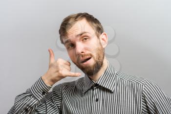 Young man with striped shirt over grey background. Doing a telephone gesture with his hand