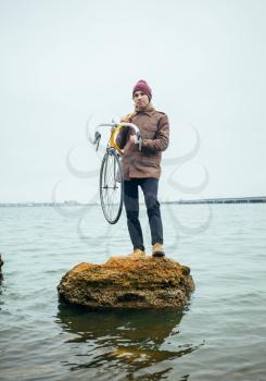 a young man with a bicycle stands on stone in lake