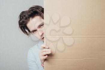 young man peeping from behind a cardboard