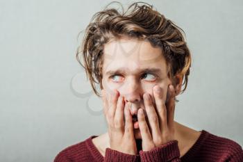 Man thinks upset with his hands to his mouth. On a gray background.