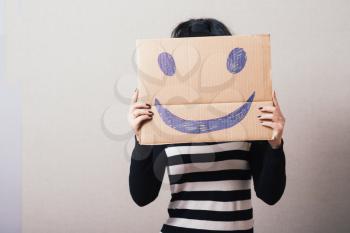 Woman with brown cardboard smiley. Gray background