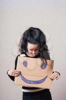 Woman with brown cardboard smiley. Gray background