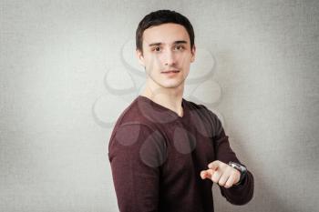 portrait of a young man pointing with his finger against a grey background