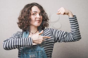 Woman playfully shows the muscles in the hand. On a gray background.