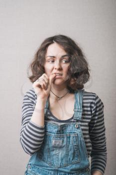 The woman lost in thought, chewing on nails from experiences fear. On a gray background.