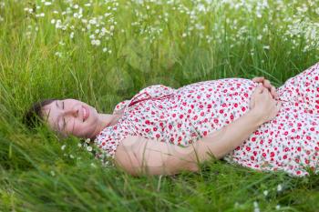 Pregnant woman with closed eyes lie in chamomile and grass background
