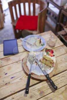 Strawberry cake on wooden table with knife, fork, tablet pc in the cafe