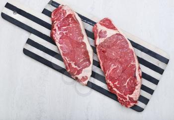 Raw new york strip steaks on a cutting board