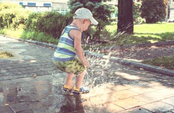 Little boy jumping in puddle. Summertime playground