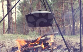 Touristic kettle on fire of burning campfire in camping in the hike. Cooking food in forest on wooden firewood.