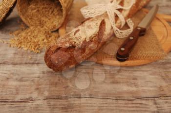 Homemade baked rye long loaf on wooden background with grains and knife