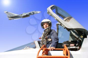 The military pilot in the plane in a helmet in dark blue overalls against the blue sky