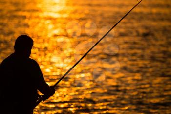 Fisherman with a fishing rod at sunset .