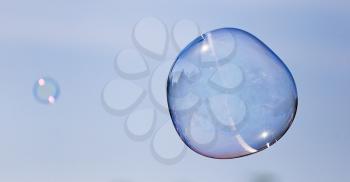 Big soap bubble against the blue sky .