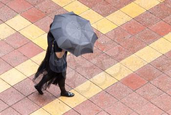 Girl with umbrella walking along paving stones .