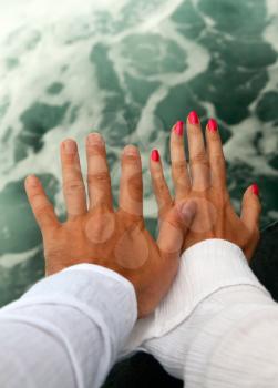 Men's and Women's tanned hands against the raging sea