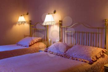 Trendy hotel in pink with two beds, in the light of the bedside lights and cold light from the window.