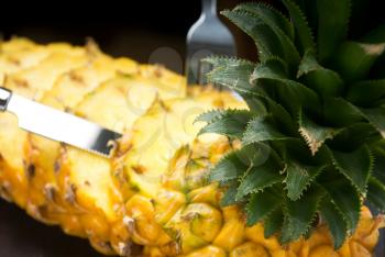 ripe vibrant pineapple sliced on a black plate with knife and fork