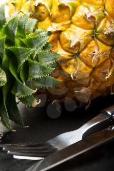 ripe pineapple on a black plate with knife and fork