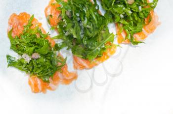 fresh salmon carpaccio sushi sashimi with arugula rocket salad and caper on top