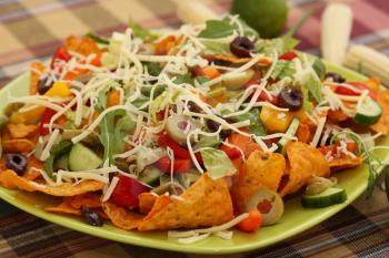 Heap of nachos with vegetables on green plate.