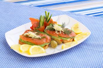 Sandwiches with salmon, cheese, lettuce,  herbs on plate, olives and lemons.