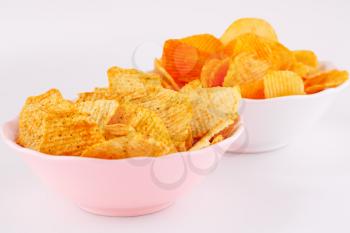 Potato chips in pink and white bowls isolated on gray background.