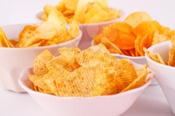 Potato and wheat chips in bowls on gray background.
