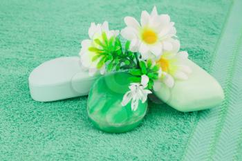 Colorful soaps and flowers on green towel.