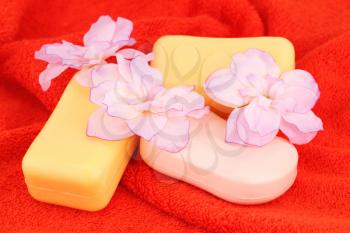 Colorful soaps and flowers on red towel.