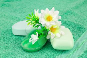 Colorful soaps and flowers on green towel.