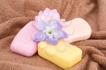 Colorful soaps and flowers on brown towel.