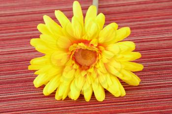 Yellow fabric daisy on striped cloth background.