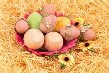 Easter colorful eggs in basket and flowers on straw background.