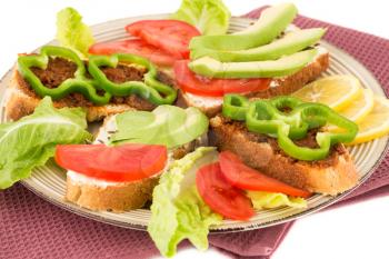Sandwiches with cheese, sundried tomatoes, pepper, avocado and seeds, lettuce, lemon on beige  plate on towel on white background.