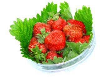 A heap of fresh strawberries in glass bowl on green foliage . Isolated