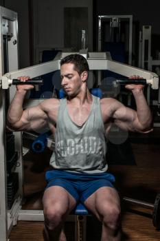 young bodybuilder doing shoulder press on machine