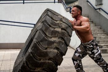 A muscular man participating in a cross fit workout by doing a tire flip