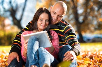 Beautiful Couple Sitting In Park And Using Tablet Computer