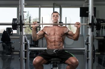 Muscular Young Man Doing Heavy Weight Exercise For Shoulders In Gym