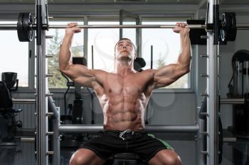 Muscular Young Man Doing Heavy Weight Exercise For Shoulders In Gym