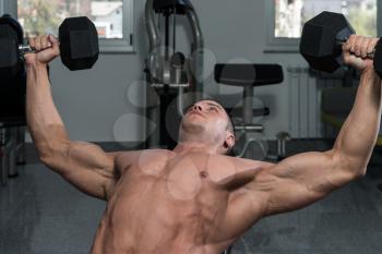 Young Man In Gym Exercising Chest With Dumbbells