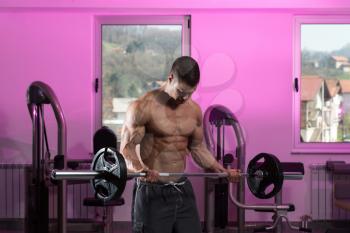Young Athlete Doing Heavy Weight Exercise For Biceps With Barbell - On A Pink Background