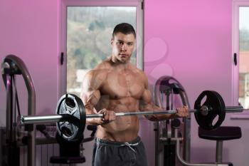 Young Athlete Doing Heavy Weight Exercise For Biceps With Barbell - On A Pink Background
