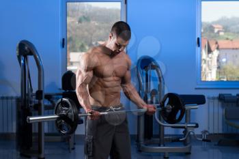 Young Athlete Doing Heavy Weight Exercise For Biceps With Barbell - On A Blue Background