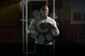 Portrait Of A Man In Jeans Holding Weights In Hand In A Dark Gym