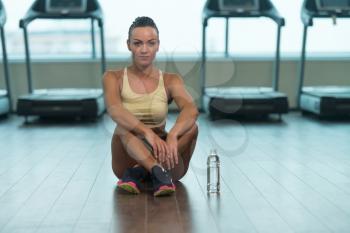 Fitness Woman Resting On Floor After Exercise And Drinking From Bottle Of Water