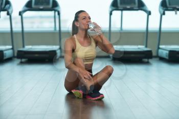 Fitness Woman Resting On Floor After Exercise And Drinking From Bottle Of Water