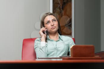 Beautiful Young Business Woman Sitting At Office Desk And Talking On Cell Phone - City Businesswoman Working